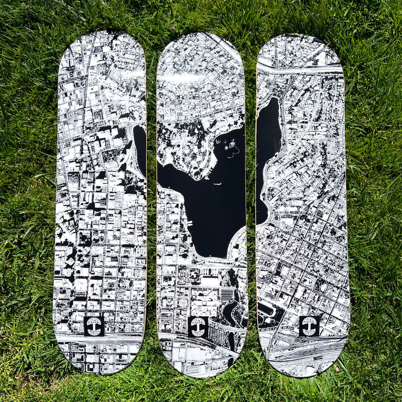 Three black and white skateboard decks with an aerial image of Oakland and Lake Merritt on grass.