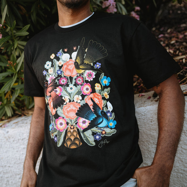 Close up from waist to chin of man wearing a black t-shirt with a graphic of flowers and birds designed by artist Jet Martinez.