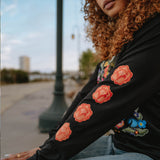 Close up of a woman’s arm wearing a long sleeve black t-shirt with four flowers designed by artist Jet Martinez. 