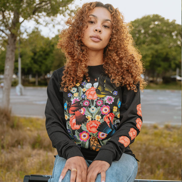 Women sitting on a park bench in a long sleeve black t-shirt with flower & bird graphic by artist Jet Martinez.