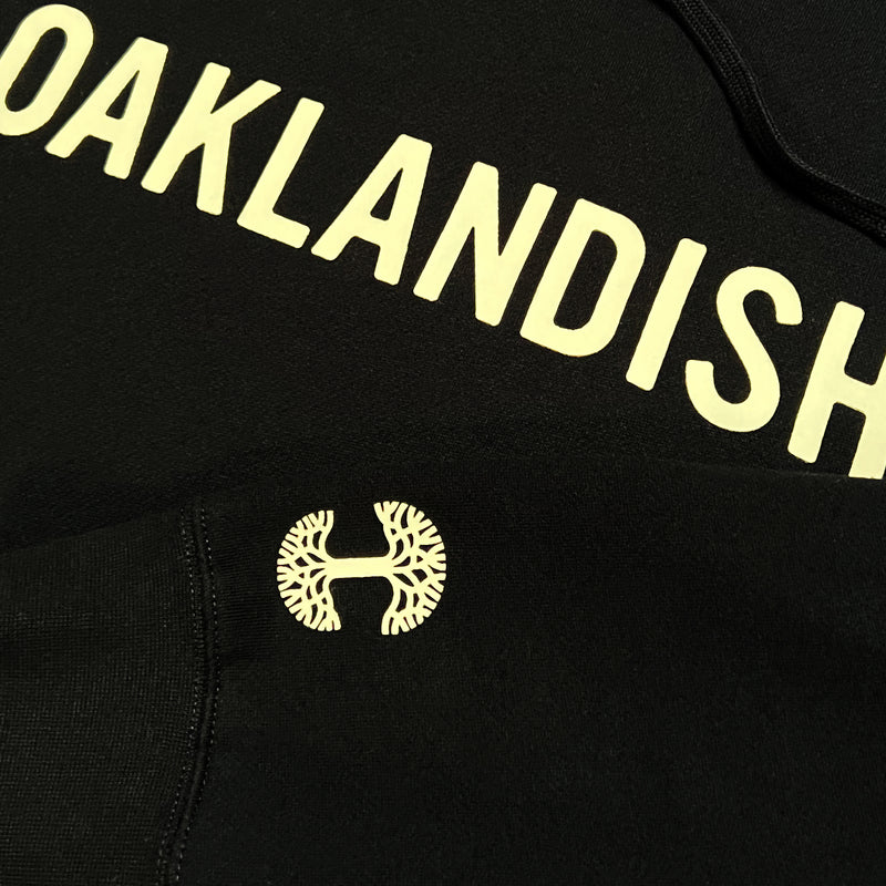 Close-up of yellow Oaklandish wordmark tree logo on a black hoodie.