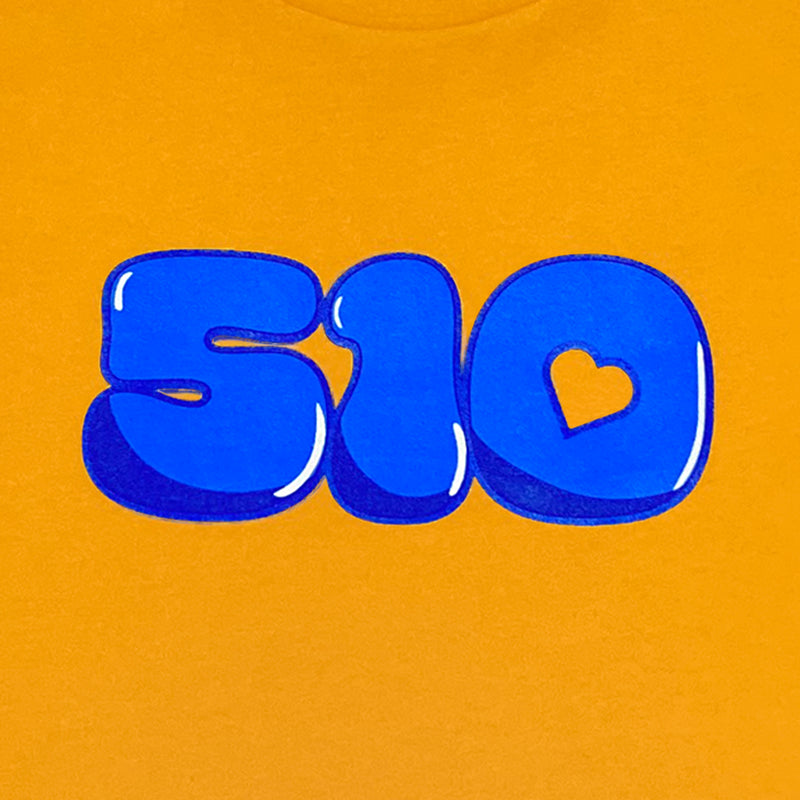Detailed close-up of blue bubble '510' graphic with the negative space in the '0' shaped like a heart on a gold toddler t-shirt.