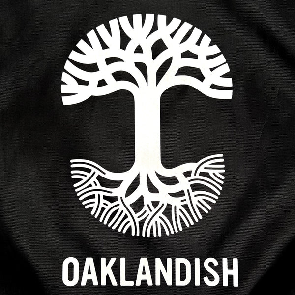 Detailed close-up of the white Oaklandish tree logo and wordmark on a black polyester drawstring cinch bag