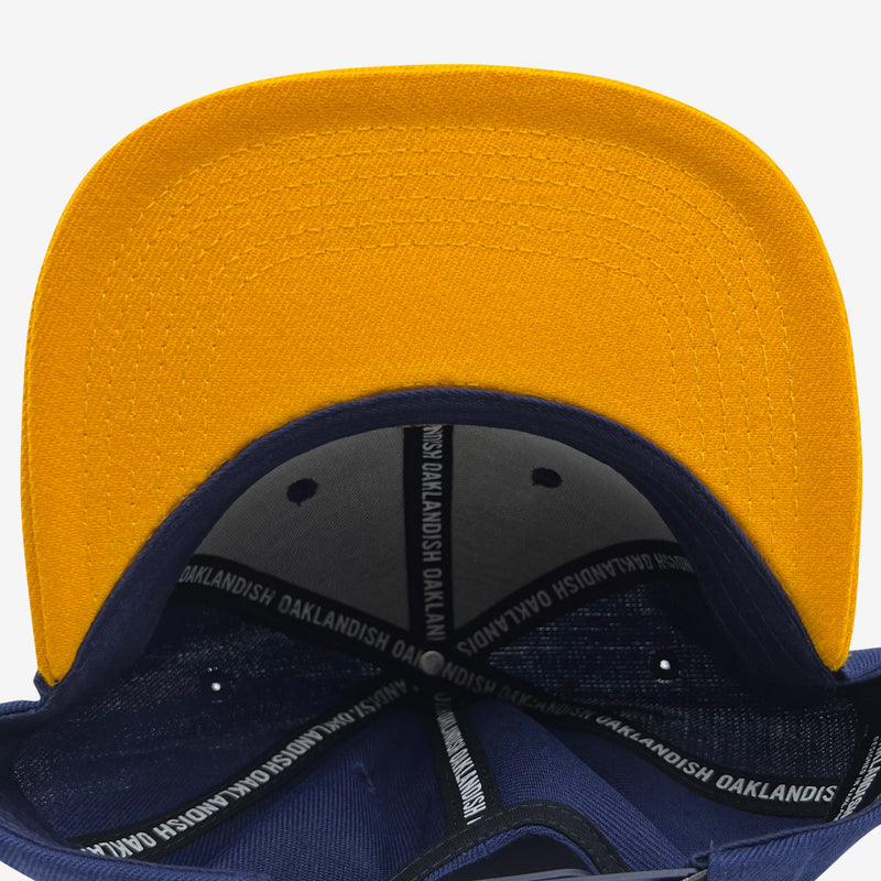 Yellow flat under brim angle with Inside royal blue snapback hat crown with ‘OAKLANDISH’ wordmark on black striping .