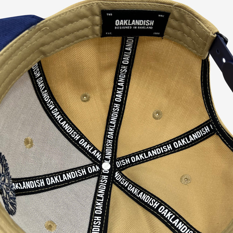 Inside tan snapback hat crown with ‘OAKLANDISH’ wordmark on black striping and Oaklandish patch.