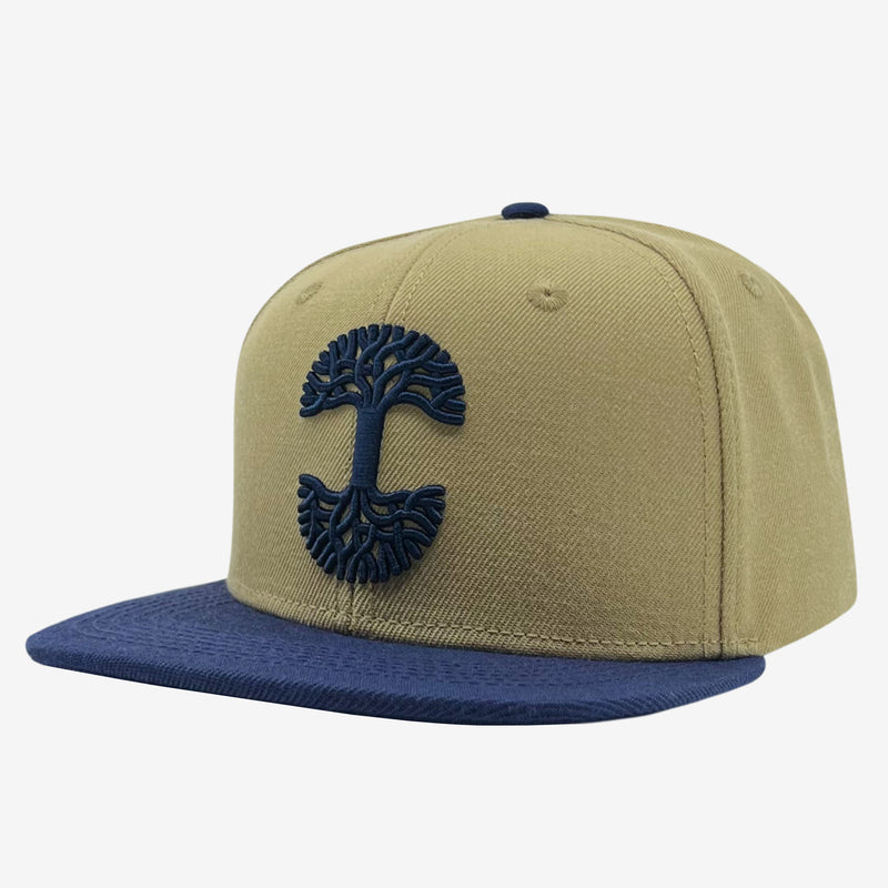 Side view of tan snapback hat with navy embroidered Oaklandish tree logo on crown and contrasting navy brim.