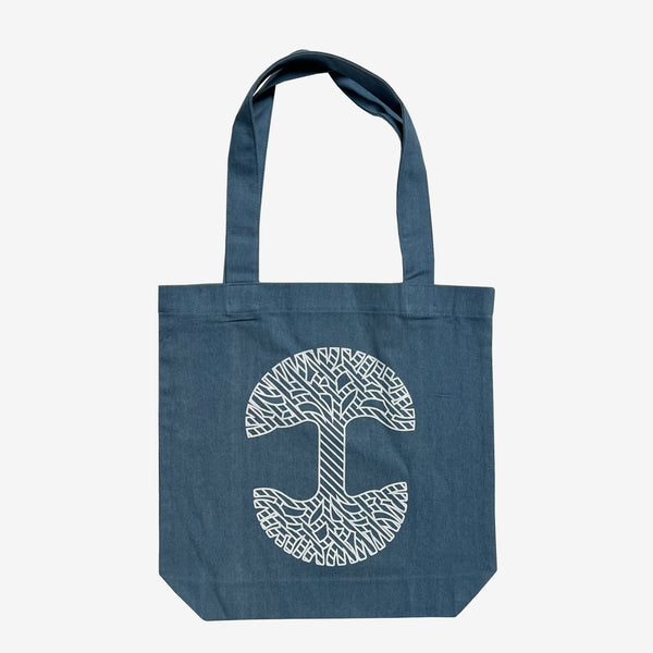 The back side of a blue denim cotton shopping tote bag with a white Oaklandish tree logo.