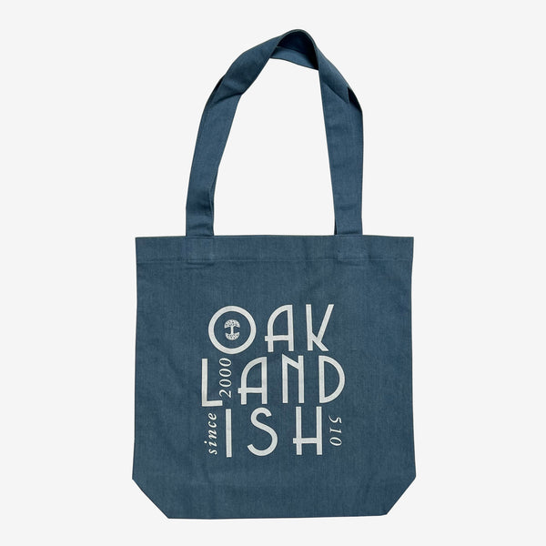 The front side of a blue denim cotton shopping tote bag with Oaklandish 510 Since 2000 wordmark and tree logo.