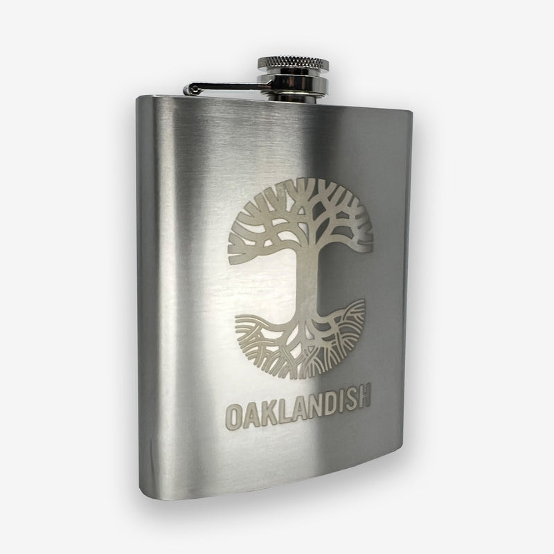 Side view of silver 8 oz hip flask with screw top lid and gold Oaklandish tree logo and wordmark.