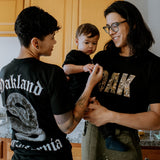 Male model wearing black floral 'OAK' tee with family indoors.
