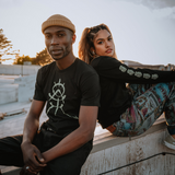 A man and a woman are sitting outdoors wearing short and long sleeve  t-shirts from the GATS X Oaklandish collection.