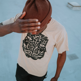Man wearing a mushroom brown boxy cut t-shirt with an oversized black GATS mask silhouette on the chest.