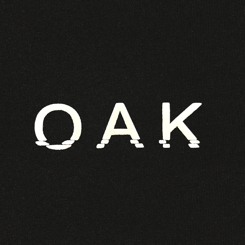 Close-up of OAK wordmark in white puff ink on a black t-shirt.