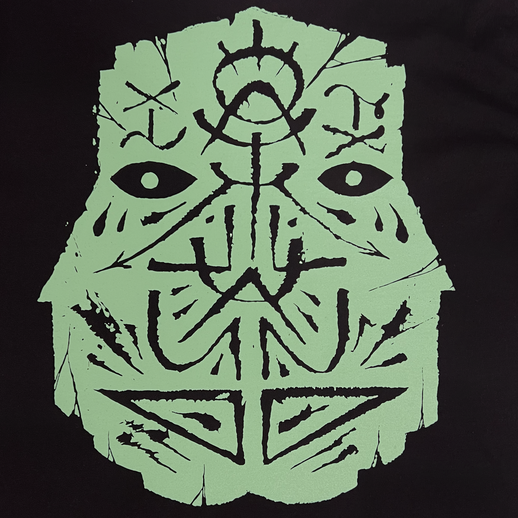 Detailed close-up of large teal GATS mask silhouette on a black long-sleeve t-shirt.