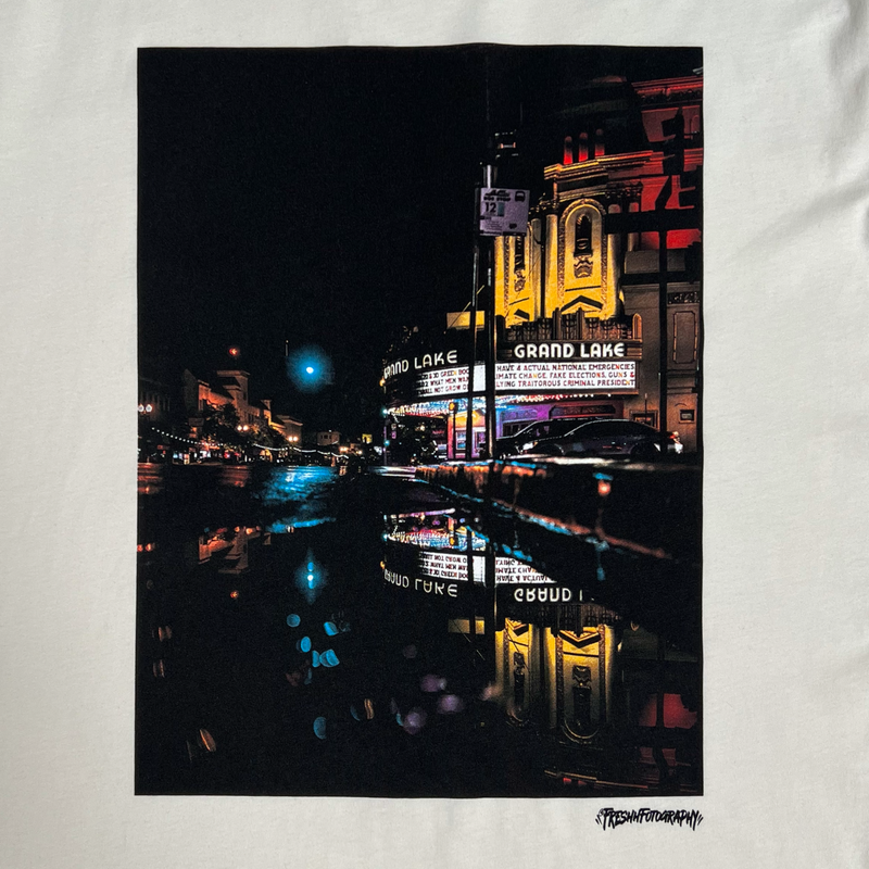 Close up view of short sleeve natural t-shirt with image of a rainy night reflecting street lights and The Grand Laker Theatre.