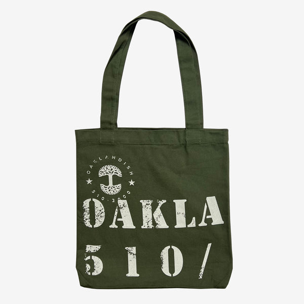 The front side of an olive green cotton shopping tote bag with capitalized OAKLA and tree logo.