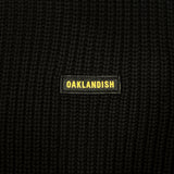 Detailed close-up of embroidered Oaklandish wordmark woven label patch on a black heavy-knit sweater.