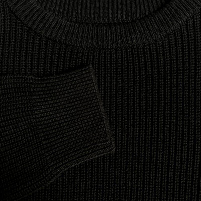 Detailed close-up of chest and cuff of a heavy knit sweater in black.