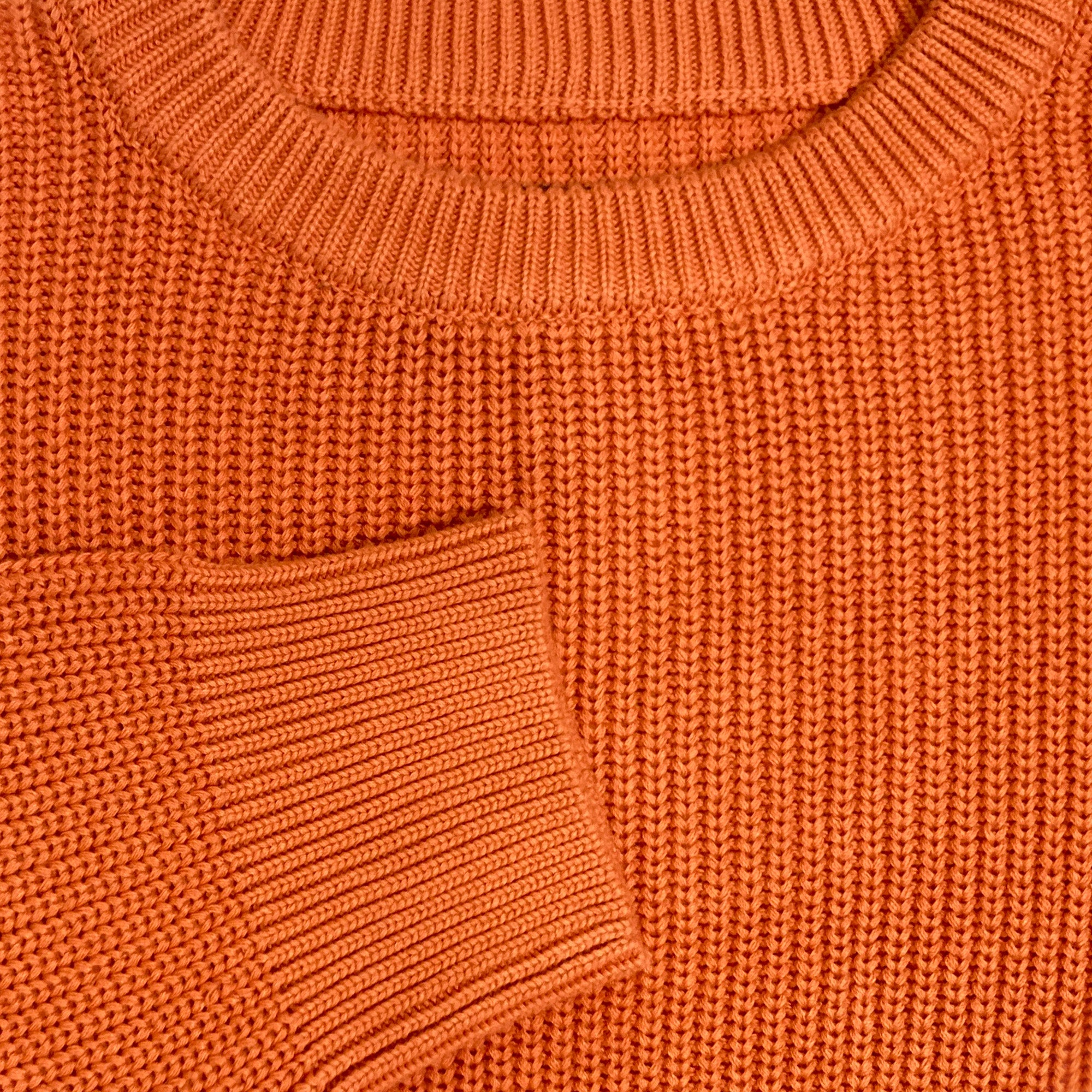 Detailed close-up of chest and cuff of a heavy knit sweater in autumn orange.