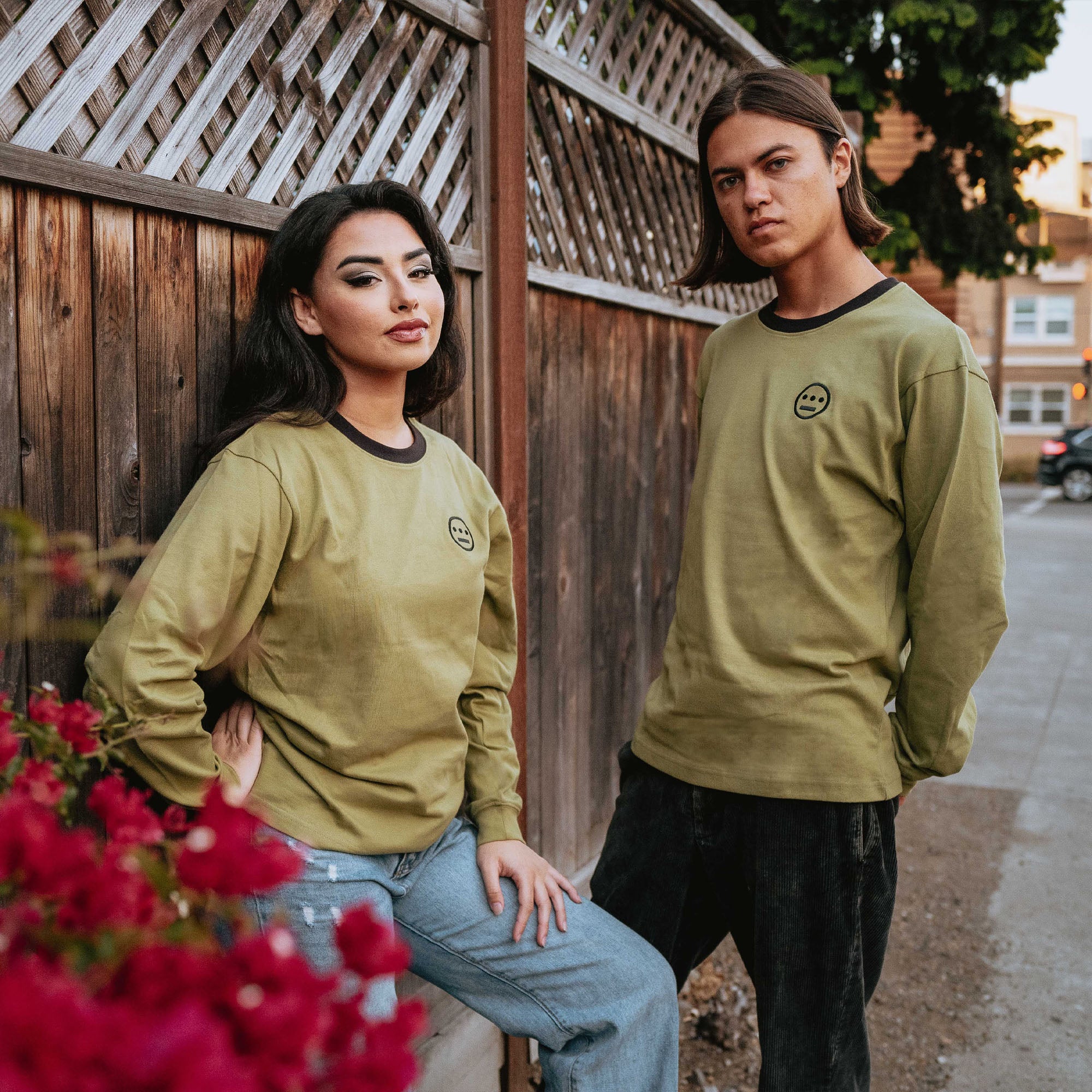 Army green long sleeve crew neck tee with black Hiero hip-hop logo on chest on man and a woman outdoors.