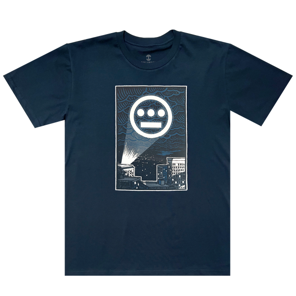 The front side of a navy t-shirt with a graphic of Hiero logo spotlight signal in Oakland’s night sky above buildings.