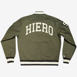 The backside of an army green cadet jacket with a large cream-colored Hiero wordmark. 