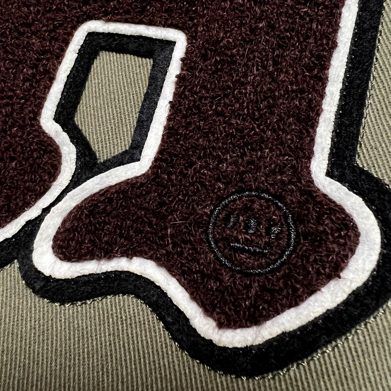 Detailed close-up of large chenille 'H' patch with small embedded round Hiero logo on left wear side chest of army green cadet jacket.