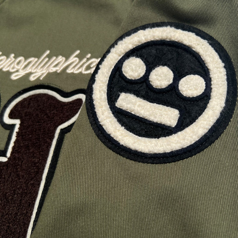Detailed close-up image of chenille Hiero logo patch on an army green cadet jacket.