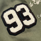 Detailed close up image of chenille 93 patch on army green cadet jacket.