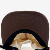 Brown under brim angle and Inside of cream snapback hat crown with ‘OAKLANDISH HIEROGLYPHICS’ wordmark on cream striping