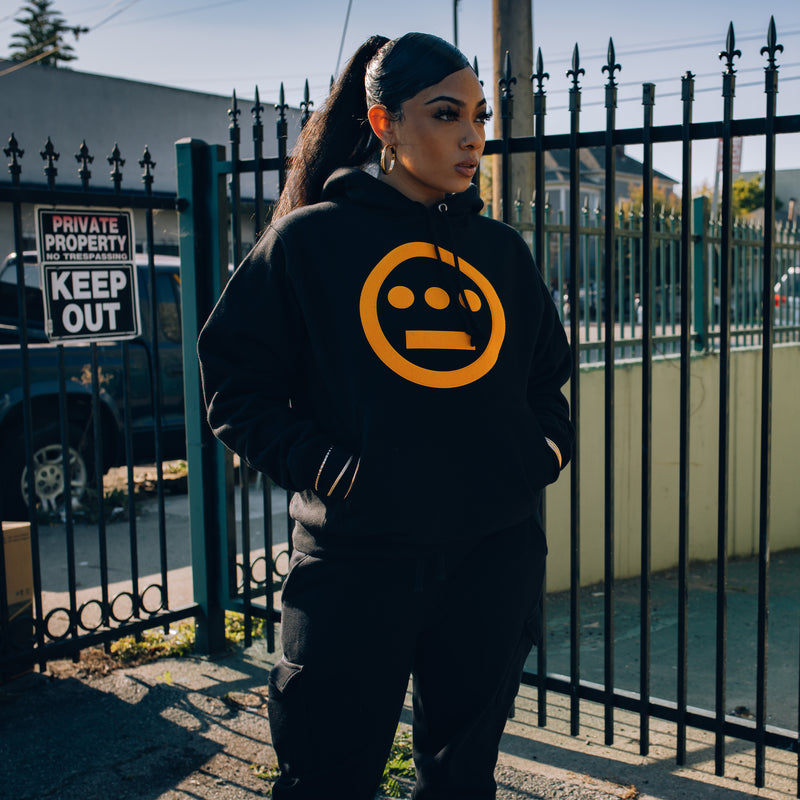 Female Model wearing champion x Hiero hoodie in black and yellow.