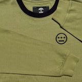 Close-up of black embroidered Heiro hip-hop crew logo and black neck trim on an army green long-sleeve t-shirt. 