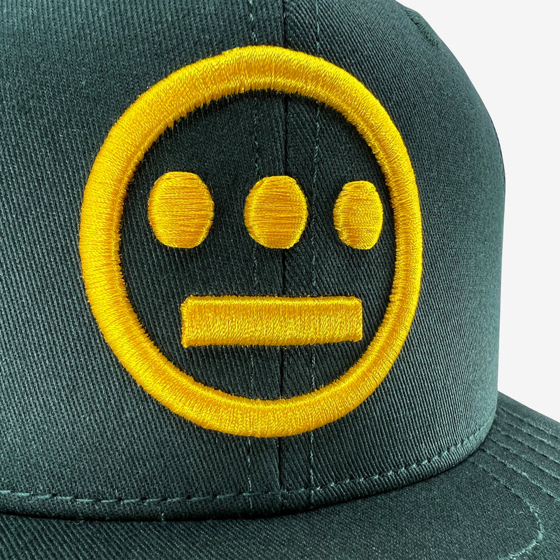 Close-up of embroidered gold Hieroglyphics hip-hop logo on a green cap.