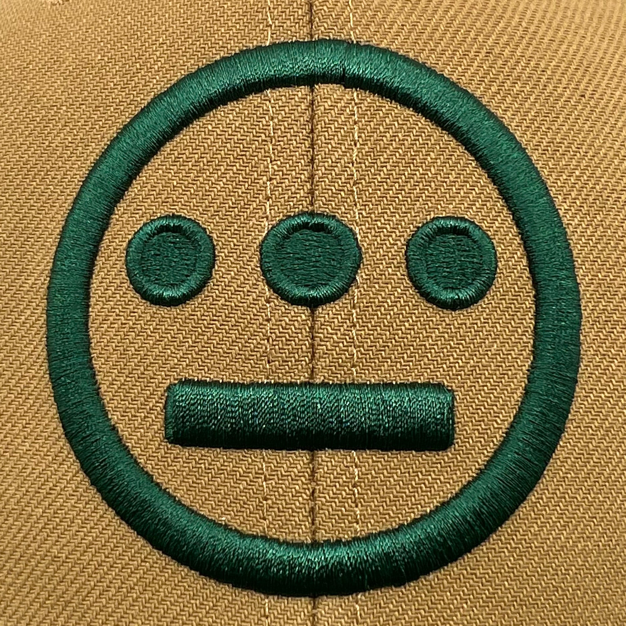 Detailed close-up of embroidered green Hiero hip hop logo on a brown Mitchell & Ness cap.