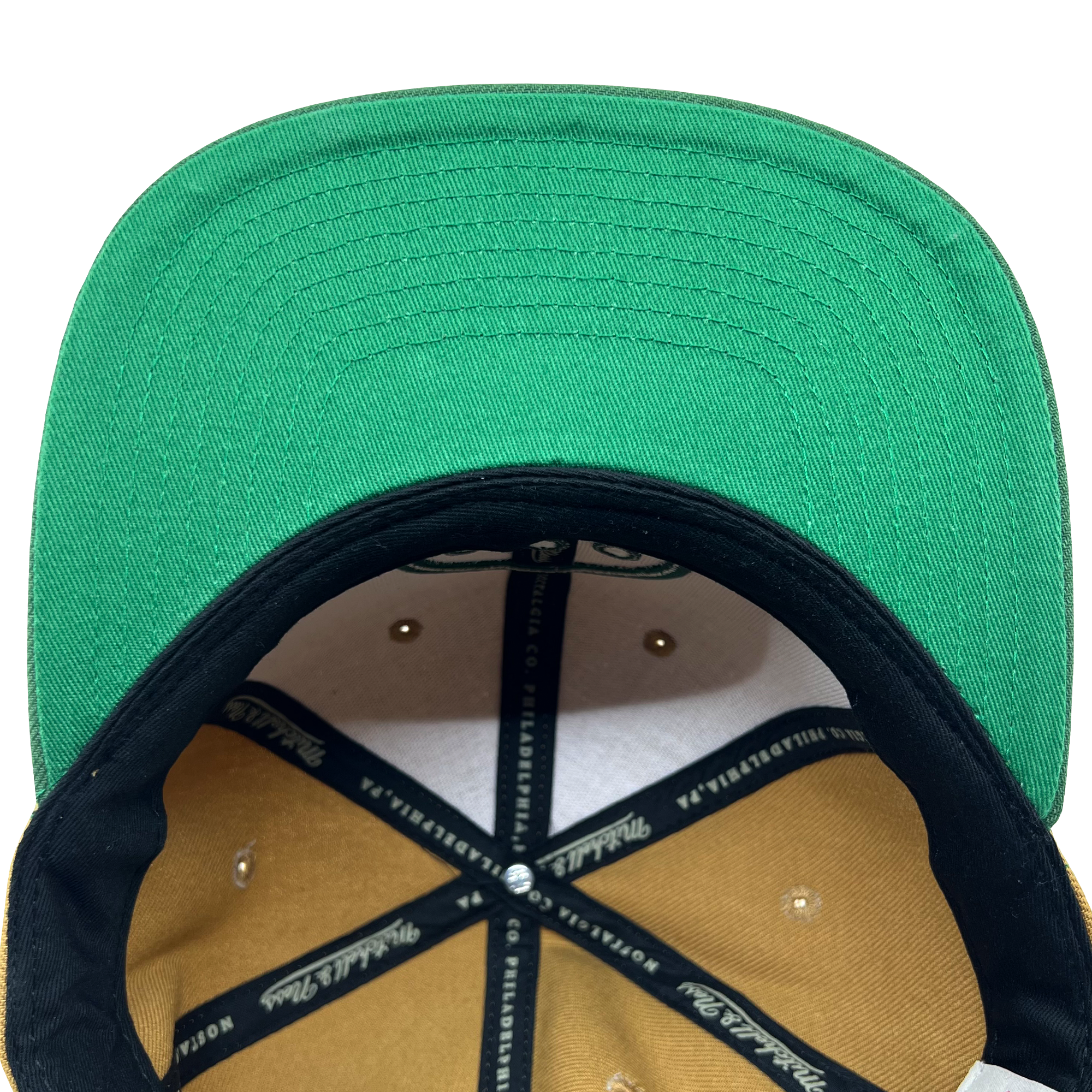 Top-down view of the inside of a Hiero BNB Logo Snapback by Hieroglyphics. The green brim is visible alongside black sweatbands featuring white text. The interior panels are tan, secured with metal rivets. The inside of the cap is structured, showcasing stitching and the underside of the green fabric.
