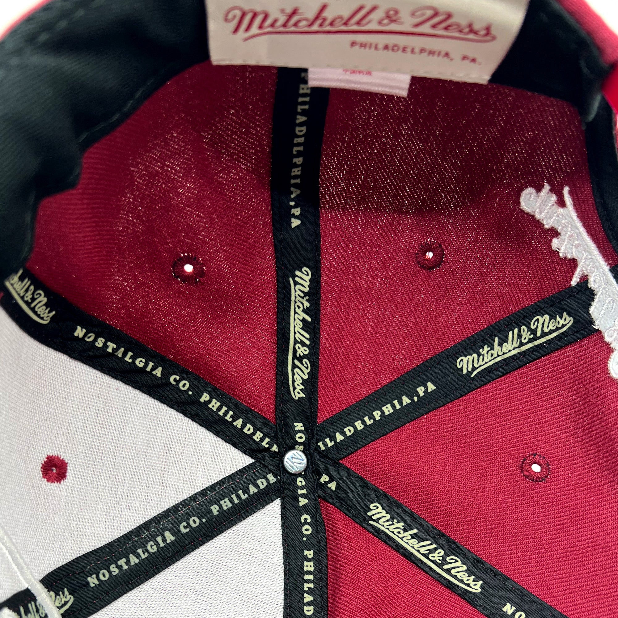 Detailed close-up of Mitchell & Ness taping inside the crown of a cardinal red cap.