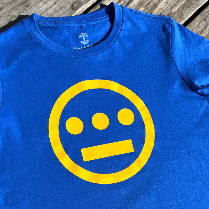Close up of yellow Hieroglyphics Hip-Hop logo on a royal blue t-shirt on picnic bench.