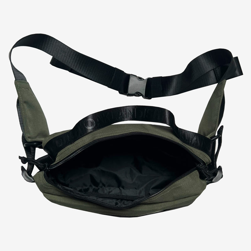 Top view of black nylon hip bag with open top zipper to expose inside of bag and top handle with an Oaklandish wordmark.