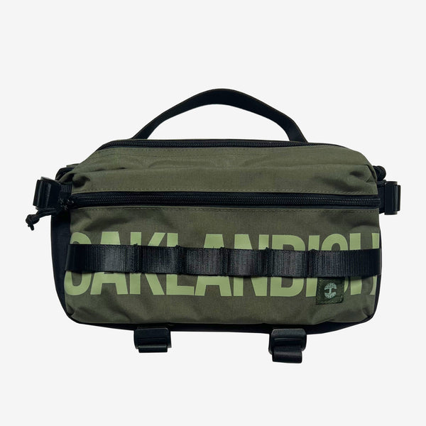 An olive nylon hip bag with a light green Oaklandish wordmark, top zipper & handle & small Oaklandish tree logo.