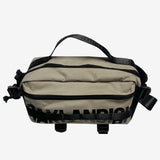A sand nylon hip bag with a black Oaklandish wordmark, front zipper, top handle, waist belt, & small white Oaklandish tree logo.