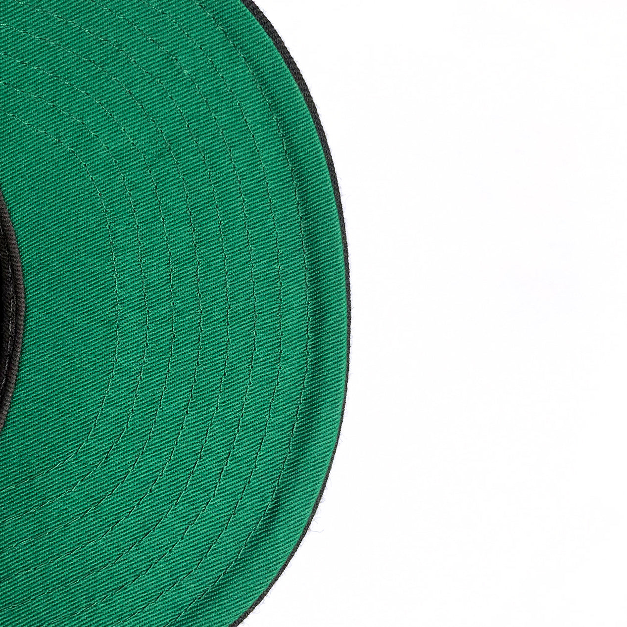 Close-up of the underside of the green brim from a New Era Oakland Roots SC 59FIFTY Fitted cap, showcasing detailed concentric stitching. The edge of the black-trimmed brim is slightly angled toward the top left corner, with the remainder of it extending out of frame to the bottom left. The background is white.