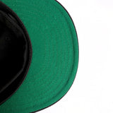 The green underside of the bill of a New Era black cap.