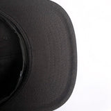 The black underside of the visor on a black snapback cap. 
