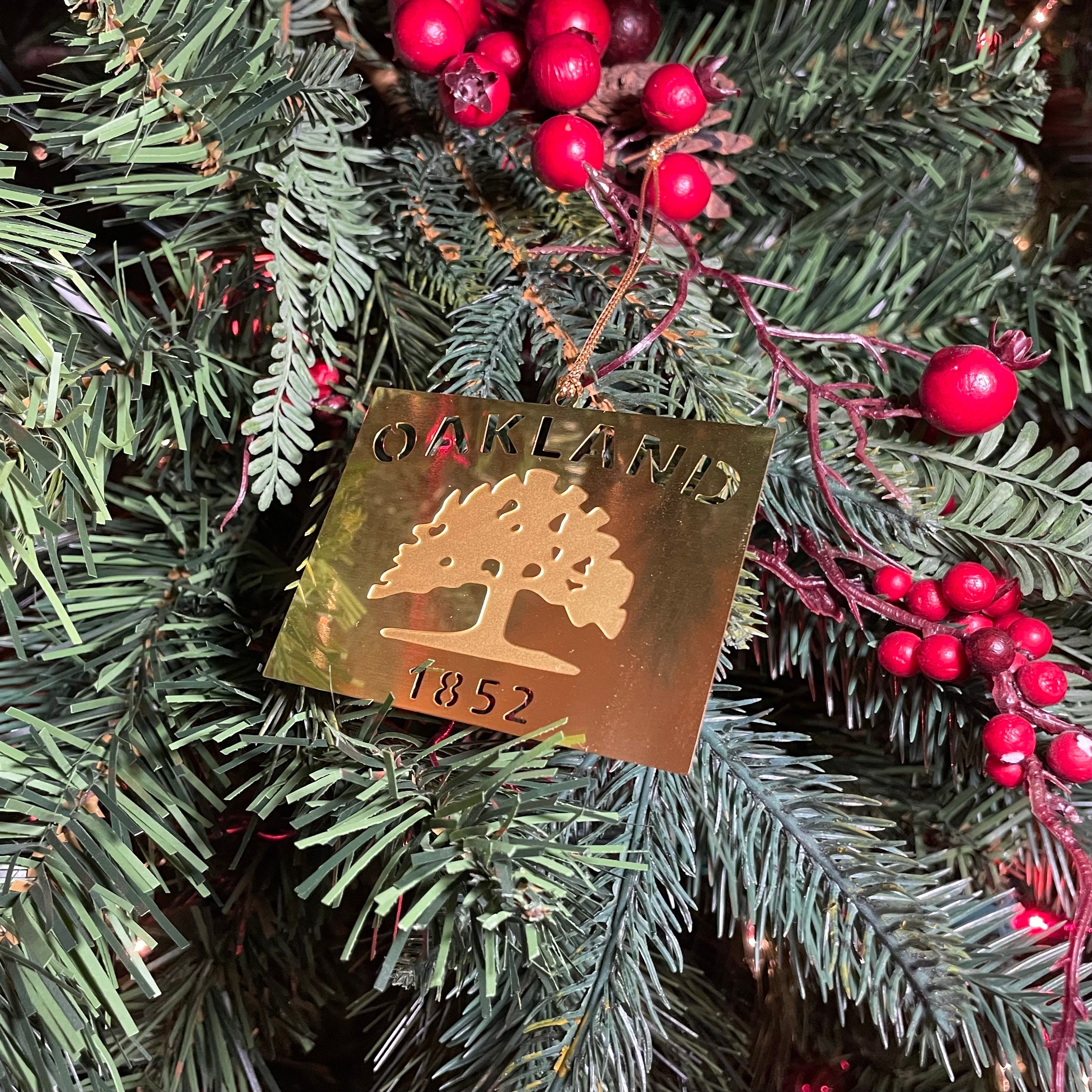 An Oakland flag is depicted in cut-out brass hanging on a decorated Christmas tree.