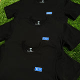 Three black t-shirts lying on grass with respective West, East North blue graphics on left breasts.