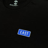 Close up of word word East in blue graphic on left breast to celebreate East Oakland on black t-shirt.