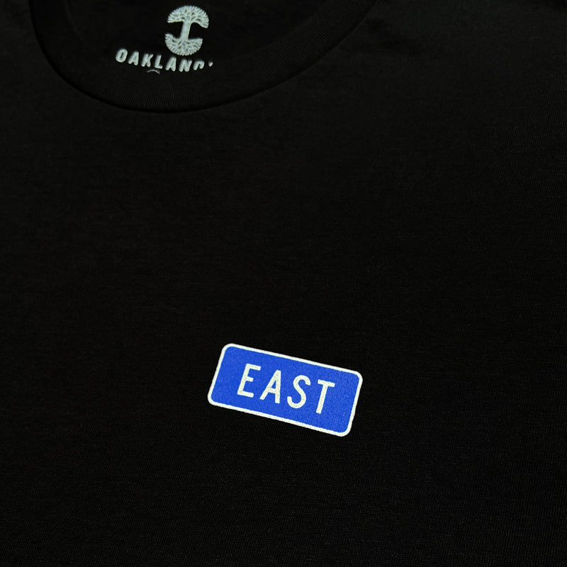 Close up of word word East in blue graphic on left breast to celebreate East Oakland on black t-shirt.