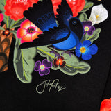 Close up of flower & bird design with artist signature on long sleeve black t-shirt designed by artist Jet Martinez. 