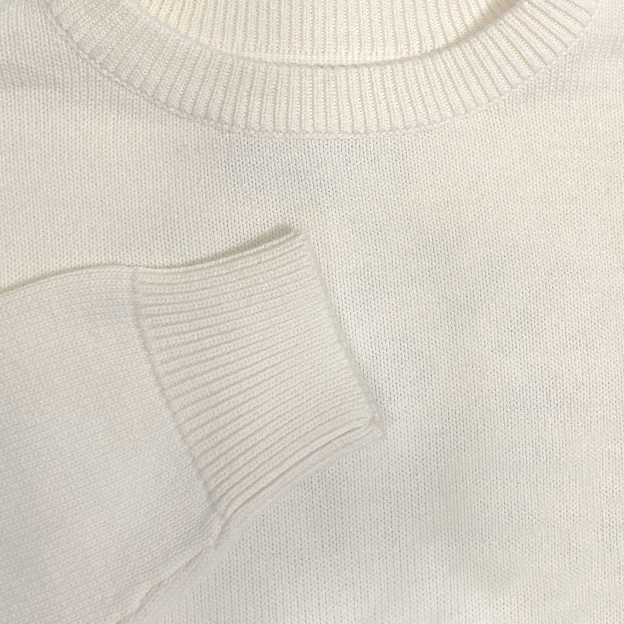 Detailed close-up of chest and cuff of a white heavy knit sweater.
