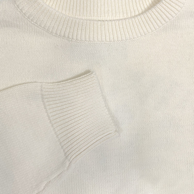 Detailed close-up of chest and cuff of a white heavy knit sweater.